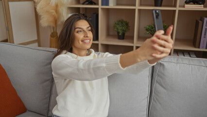 Woman smiling while taking a selfie in a cozy living room interior, capturing the essence of modern...