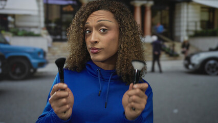 Woman closely examining two makeup brushes on street with a blurred building facade behind her; uncertainty.