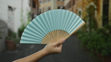 Man holding a blue fan outdoors on a city street, capturing the essence of a casual summer day in...