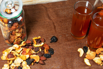 Glasses of dried fruit compote with jar and scattered fruits on brown cloth