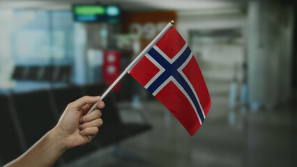 Hand holding norwegian flag in an airport terminal, showcasing a patriotic gesture indoors.