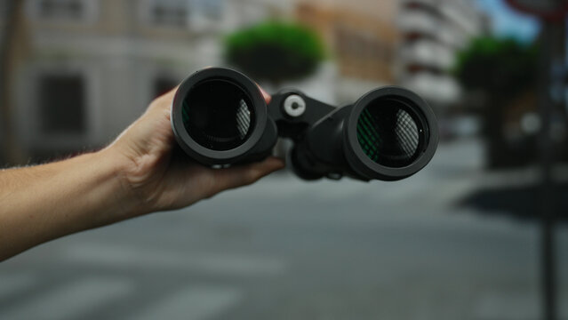 Man holding binoculars on a city street outdoors during the day, capturing urban exploration, adventure, and observation in a bustling town environment.