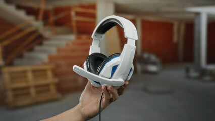 Man holding headphones at a construction site, featuring concrete background and wooden stairs,...