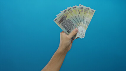 Caucasian man holding romanian banknotes fanned out against a solid blue wall backdrop emphasizing...