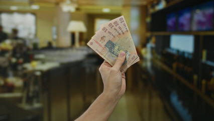 Hand displaying romanian lei banknotes in a vibrant indoor coffee restaurant setting.