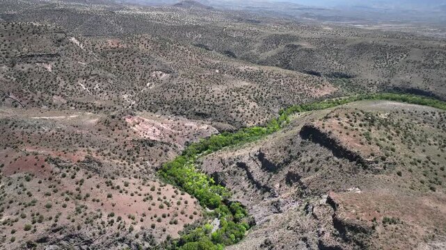 Aerial view of the winding river cutting through the arid landscape, a vibrant green vein amid the browns, West Clear Creek Wilderness, Arizona, United States.