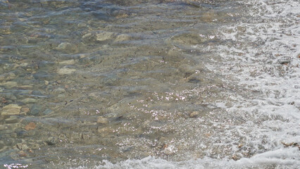 Sunlit mediterranean beach scene captures gentle waves meeting a pebbled shoreline outdoors, emphasizing natural beauty and relaxation under a clear sky.