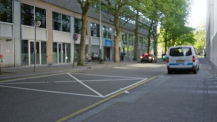 Blurred view of a european street with trees and cars in the background, capturing a defocused urban environment with a bokeh effect on an overcast day.