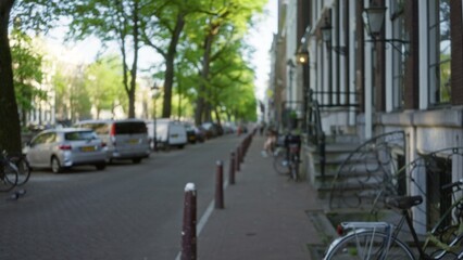 Defocused street view in a european city with blurred cars, bicycles, and trees, showcasing an outdoor cityscape with a calm, inviting ambiance on a sunny day.