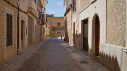 Fototapeta premium Blurred view of a quiet mediterranean old town street, with sunlit stone buildings and a distant bokeh effect, evoking a sense of serene urban wanderlust.