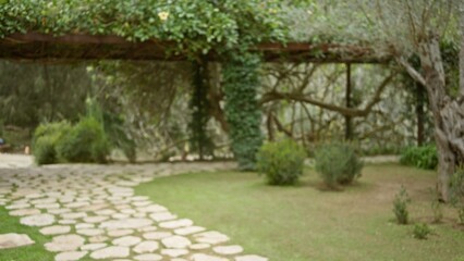 Mediterranean garden with lush greenery and a defocused stone path, creating a serene, blurred and bokeh-filled atmosphere under the dappled sunlight.