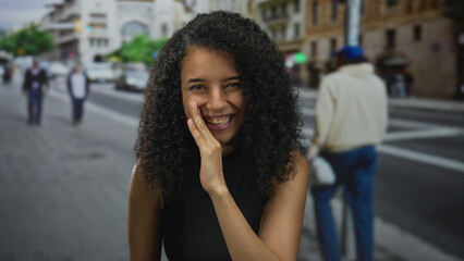 Young hispanic woman wearing sleeveless black top smiling with finger to lips for silence on busy...