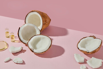 Open coconuts with small vials of oil on a pink background, representing skincare, aromatherapy, and natural cosmetic ingredients. Space for product presentation