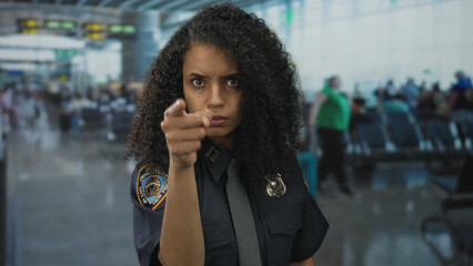 Woman in navy uniform, police officer, standing commandingly inside a bustling airport terminal...