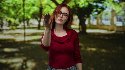 Woman pointing assertively at the camera in an outdoor park setting, with red hair and glasses,...