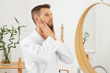 Handsome young man applying essential oil for beard in bathroom