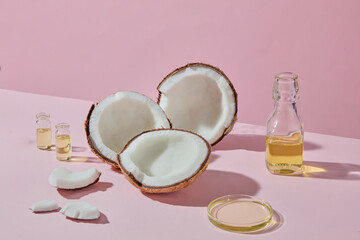 Coconut halves and a small glass bottle of oil arranged on a pink table, highlighting coconut as a source of natural beauty and wellness.
