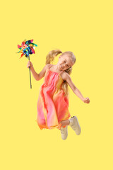 Cute little girl with toy windmill jumping on yellow background