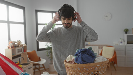 Young man listening to music while folding laundry in a bright, homey room, showcasing a relaxed...