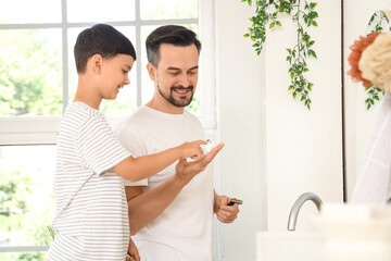 Happy father and his little son applying shaving foam and razor in bathroom