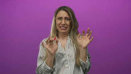 Middle aged woman wearing glasses recoils in purple studio setting with hands raised in defensive...