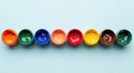 Top view of colorful paint pots arranged in a line on a light blue background