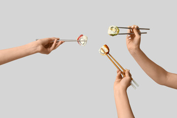 Female hands holding chopsticks with different tasty sushi rolls on grey background
