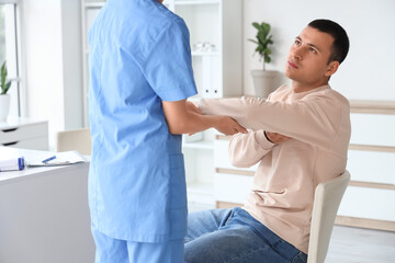Obraz premium Young man with pain in his elbow visiting doctor at hospital