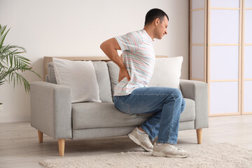 Fototapeta premium Young man suffering from back pain on sofa at home