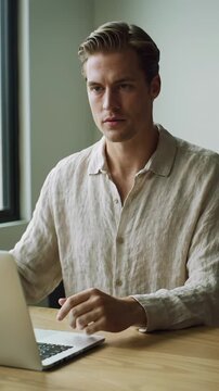 A young caucasian man in a modern beige shirt works intently on his laptop at a minimalist desk in a contemporary home office. Slow dolly-in to his face reveals a shift to profound clarity and
