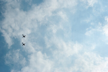 Two small airplanes flying in clear blue sky with white clouds