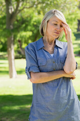 Senior woman holding right hand to temple while folding left arm across chest in sunlit park