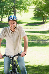 Middle-aged man wearing bicycle helmet sitting on bicycle in park monitoring cycle computer
