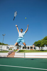 Mid adult male tennis player jumping for ball with racket on outdoor court near net