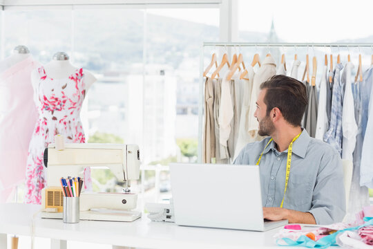Sewing machine humming on desk with laptop and swatches near mannequins by windows overlooking city
