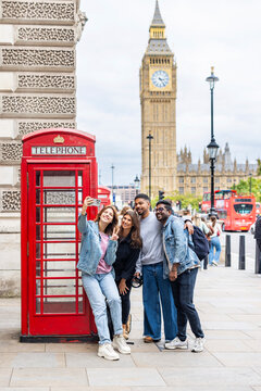 Happy tourists taking a selfie by red telephone booth and Big Ben in London