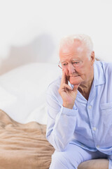 Senior man sitting on bed with blanket in pajamas resting on hand in bedroom, copy space