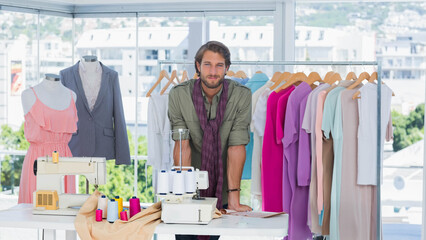 Male fashion designer leaning on white worktable in bright design studio with two sewing machines