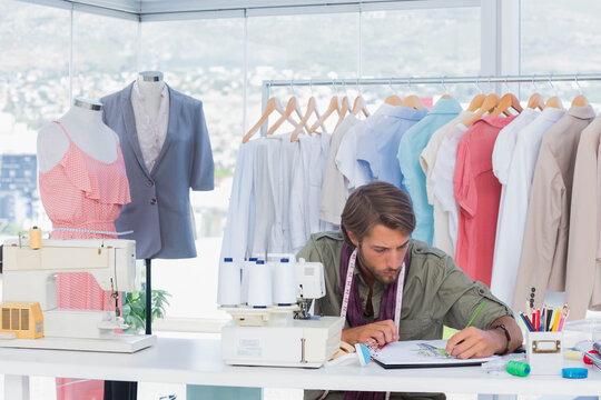 Male fashion designer sketching in notebook at design studio with sewing machines, copy space