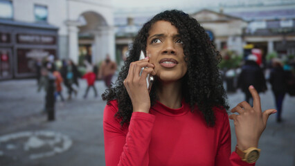 African american woman holds smartphone to ear with raised hand under overcast sky on crowded urban...