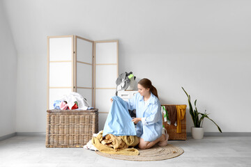 Young woman sorting dirty clothes near washing machine in laundry room