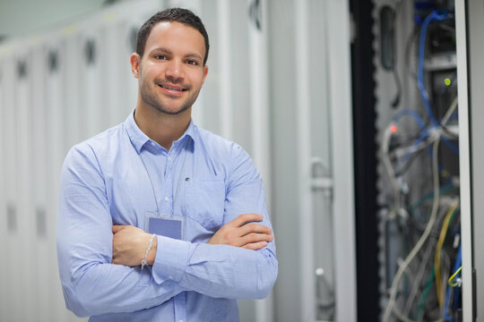 Male IT technician standing with arms crossed in data center server cabinets and cables, copy space