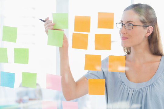 Mid adult female moving sticky note on glass board in meeting room with pen, copy space