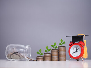 Study goals, Red alarm with graduation hat, Glass bottle and plants growing up on stack of coins....