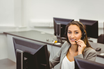 Female call center operator in grey blazer answering calls at office desk with headset, copy space