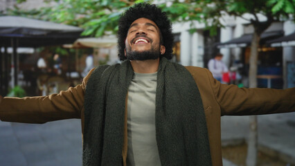 African american man smiling joyfully on a city street with arms outstretched in a relaxed outdoor setting.