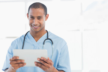 African American male healthcare worker holding tablet and smiling in clinic with stethoscope