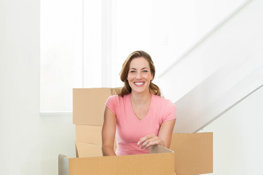 Woman smiling while unpacking moving boxes inside modern home near staircase with natural light - Powered by Adobe