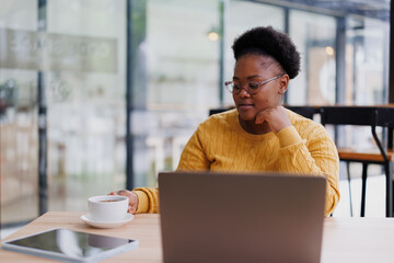 Focused businesswoman working remotely, savoring a cup of tea while engaging with her laptop in a...