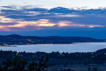 Dramatic pre-dawn view from the Tihany lookout towards Balatonfured, with a cloudy sky illuminated in orange where the horizon is clear.